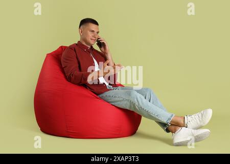 Handsome man talking by smartphone on red bean bag chair against green background Stock Photo