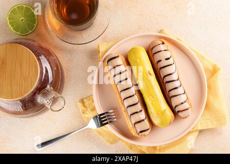 Different tasty glazed eclairs and tea served on color textured table, flat lay Stock Photo