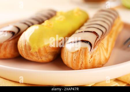 Plate with different tasty glazed eclairs on table, closeup Stock Photo
