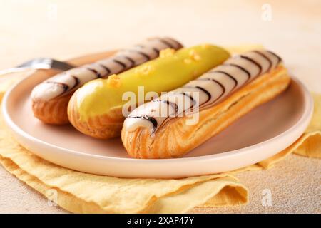 Different tasty glazed eclairs served on color textured table, closeup Stock Photo