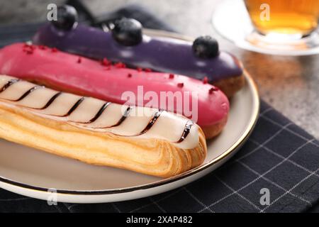 Plate with different tasty glazed eclairs on table, closeup Stock Photo