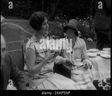 A Group of People Drinking Tea and Eating Cakes in the Garden, 1926. From &quot;Time to Remember 1926 - Short Sharp Shower&quot;- Reel 1; a documentary about 1926 - General Strike, international politics, dancing, weather and record breaking feats. Stock Photo