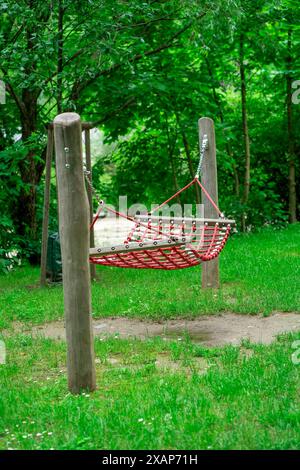 Large red hammock suspended on logs in a city park. Stock Photo