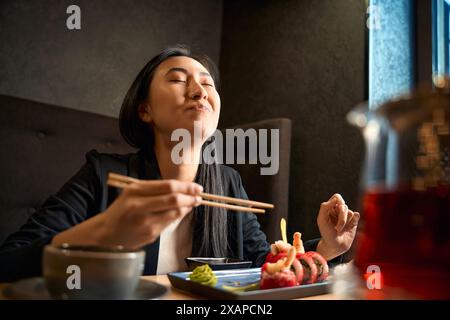 Excited Asian woman eating tasty sushi set with shrimps and tobiko roe Stock Photo