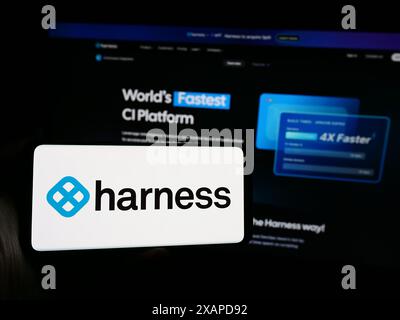 Person holding smartphone with logo of US software delivery platform company Harness Inc. in front of website. Focus on phone display. Stock Photo