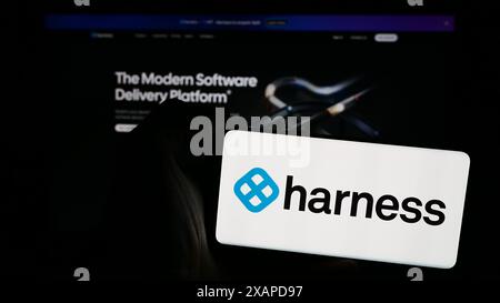 Person holding mobile phone with logo of American software delivery platform company Harness Inc. in front of web page. Focus on phone display. Stock Photo