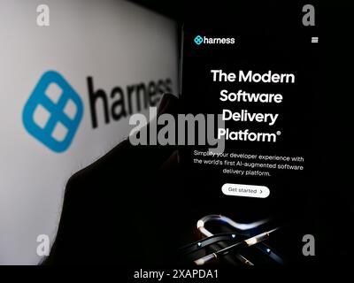 Person holding smartphone with webpage of US software delivery platform company Harness Inc. in front of logo. Focus on center of phone display. Stock Photo