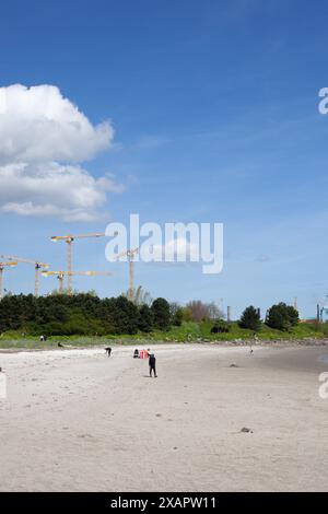 Sandymount beach on a bright, sunny day with yellow cranes in the background. There are a few clouds in the bright blue sky Stock Photo