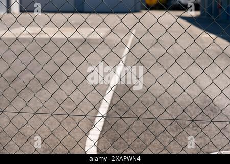 Chain link fence in front of asphalt roadd with white road markings. Stock Photo