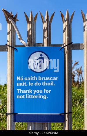 Blue, bring your litter home sign on a metal fence. There are bins, trees and grass behind the fence with a blue sky and no clouds Stock Photo