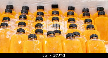 Fresh orange juice in transparent plastic bottles is soaked in ice container. Stock Photo