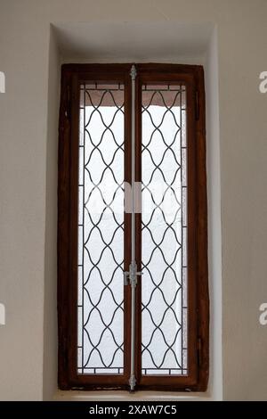 Wooden window with decorative wrought iron grating on white wall background. House interior double closed locked retro window with sill. Vertical Stock Photo