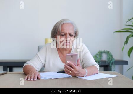 Thoughtful lady reviews important documents at home while using cell phone Stock Photo
