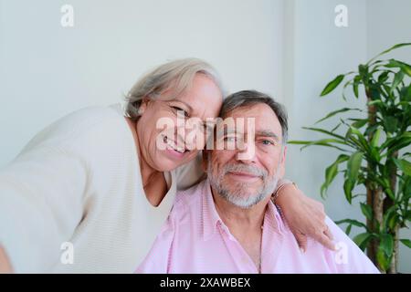 Older couple smiles while take a selfie with cell phone sitting at home Stock Photo