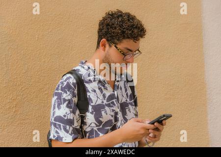 Young man with printed shirt and backpack, looking at phone. Modern style, fashion, technology, youth, communication Stock Photo