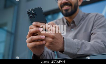 Cropped shot excited Arabian Indian man guy office manager entrepreneur employer using phone gadget addict in city outdoors happy male businessman win Stock Photo