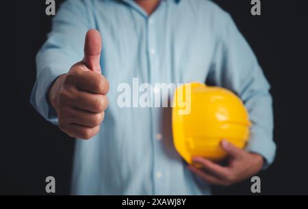 Civil engineer architect standing holding a safety helmet on dark background, Construction site plans to build high-rise buildings, Engineer building Stock Photo