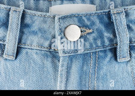 Front side of blue jeans pants with metal button closeup, macro. Denim background, texture, wallpaper, fashion concept. Design detail and seams. Stock Photo