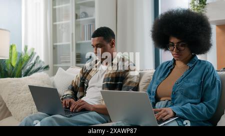 African American gadget addict couple internet addicted husband and wife social media virtual game addiction man and woman working using two laptops Stock Photo