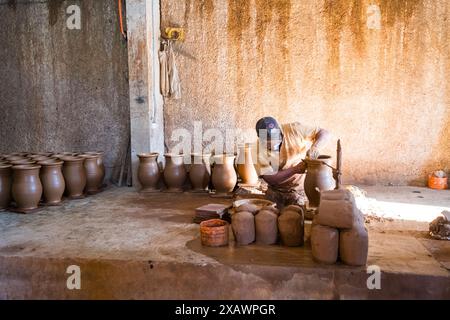 A man is working on a pottery piece in a room with many other pottery pieces. The atmosphere is calm and focused, as the man carefully shapes the clay Stock Photo