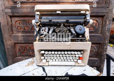 An old typewriter sits on a table. The typewriter is white and black with red keys. One can see a face due to the cerebral phenomenon of pareidolia. Stock Photo