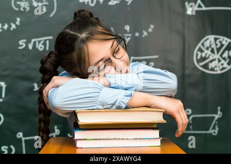 A schoolgirl with glasses fell asleep on a pile of books while sitting at the table. Stock Photo