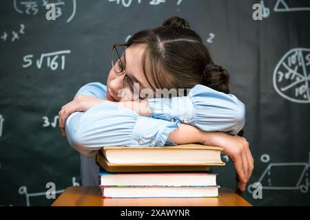 A schoolgirl with glasses fell asleep on a pile of books while sitting table. Stock Photo