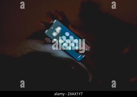 A person entering a pass code on a smart phone screen in a dimly lit environment. Stock Photo