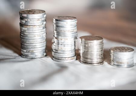 Four stacks of silver coins of varying heights arranged in a row on a white surface. Stock Photo