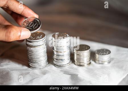 A person stacking silver coins in ascending order on a white surface. Stock Photo