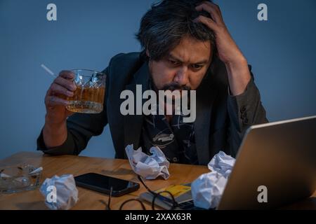 A young office worker, having failed in business, sits drinking alcohol at home Stock Photo