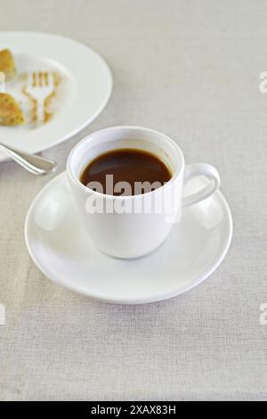 Espresso coffee white cup on a table in front of a plate of sweet. Minimalist decoration with copy space Stock Photo