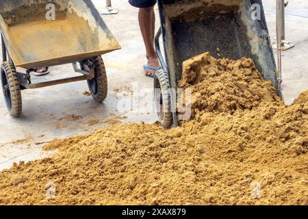 Workers dump sand from wheelbarrows onto the pile Stock Photo