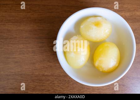 top view of three peeled raw frozen eggs in bowl on brown table Stock Photo