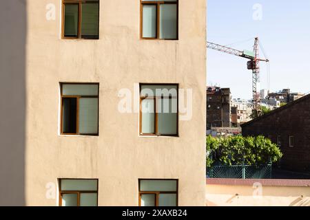 front view of yellow plastered wall of apartment house and construction crane on background in city on summer day Stock Photo