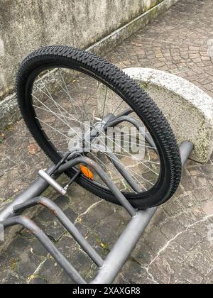 A damaged bike wheel is all that is left of a bicycle chained to a bike stand. Stolen bicycle. Chained bicycle wheel. Stock Photo
