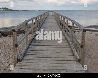 A long wooden walkway leads over the sandy beach into the sea, under a slightly cloudy sky, Eckernfoerde, Schleswig-Holstein, Germany Stock Photo