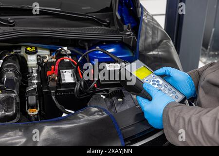 Car master mechanic checking and testing automotive battery with digital electronic battery tester and analyzer in auto vehicle workshop. Stock Photo