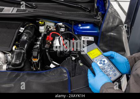 Car master mechanic checking and testing automotive battery with digital electronic battery tester and analyzer in auto vehicle workshop. Stock Photo