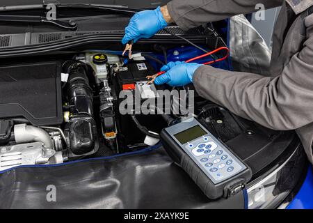 Car master mechanic checking and testing automotive battery with digital electronic battery tester and analyzer in auto vehicle workshop. Stock Photo