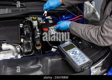 Car master mechanic checking and testing automotive battery with digital electronic battery tester and analyzer in auto vehicle workshop. Stock Photo