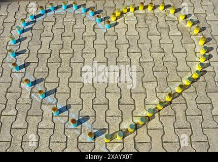 Blue and yellow candles are laid out on concrete paving stones in the shape of a heart Stock Photo