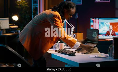 African american girl studying servers providing AI computing resources, learning to program html scripts on artificial intelligence neural network system. Woman uses coding language. Camera A. Stock Photo