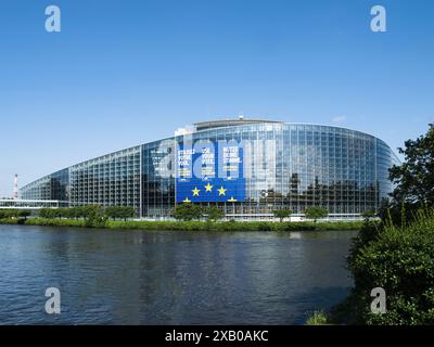 Strasbourg, France - Jun 6, 2024: The European Parliament building in Strasbourg, prominently featuring a large banner encouraging voting in the 2024 EU elections, with clear reflections on the glass facade and a calm river in the foreground. Stock Photo