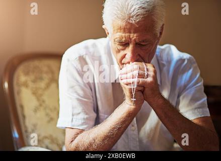Home, rosary and elderly man with praying on sofa for spiritual healing, faith or worship to God. Retirement, Christian and senior person with Stock Photo