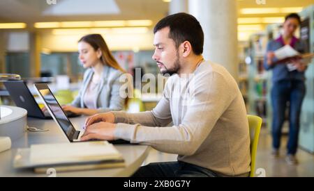 Focused young student studying with books and laptop in library Stock Photo