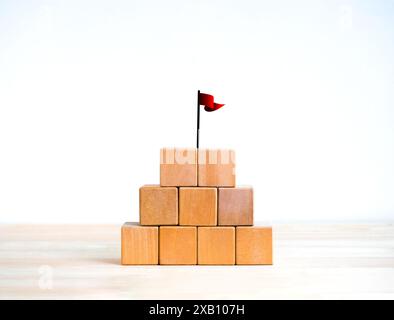 Red win flag on top of 5 wood blocks pyramid stack isolated on wooden table, white background. Empty blank template five cubes arranged for add text o Stock Photo