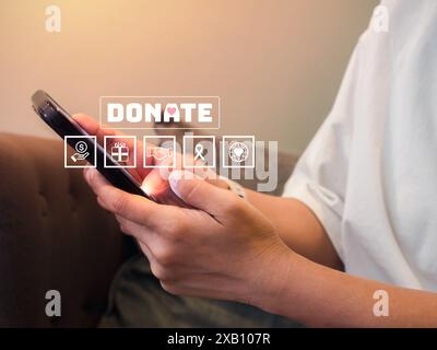 Donation online concept. Text "Donate" with charity and fundraising icons appear while female person in casual white shirt holding and using smart mob Stock Photo