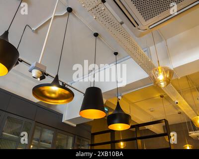 Row of various modern lights hanging from white ceiling building decorations in room, loft style. Many black vintage retro style of lamps installed in Stock Photo