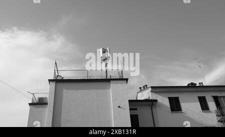 Black and white photo of a telecommunication tower standing on a building roof, contrasting against a cloudy sky Stock Photo